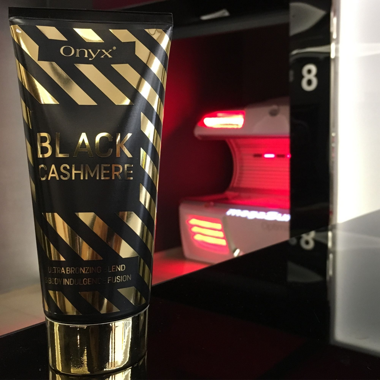 Onyx Black Cashmere tanning cream placed on a glossy surface in front of a modern sunbed glowing with red light