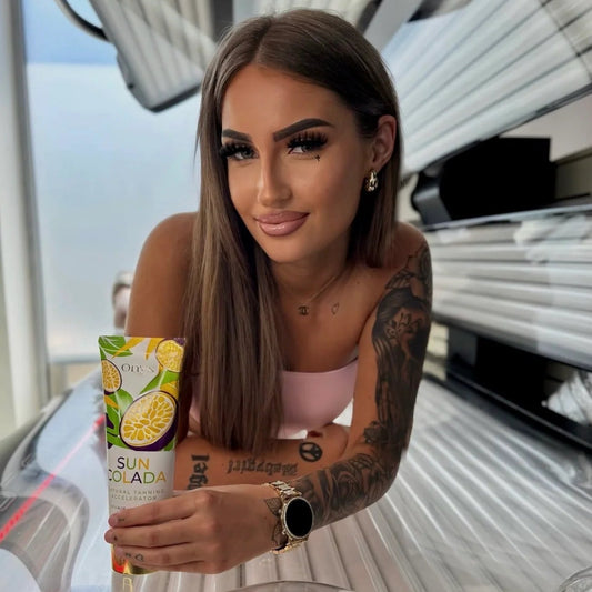 Model leaning on a sunbed and holding an Onyx Suncolada Natural Tanning Accelerator cream tube.