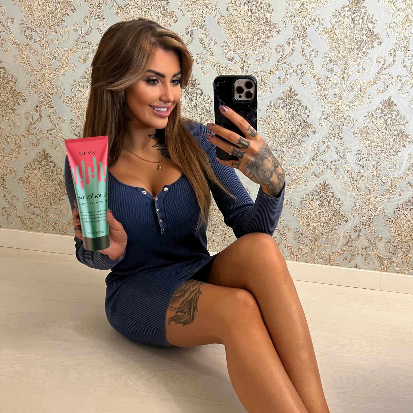Tattooed woman taking mirror selfie with Onyx Sunphoria sunbed tanning accelerator cream