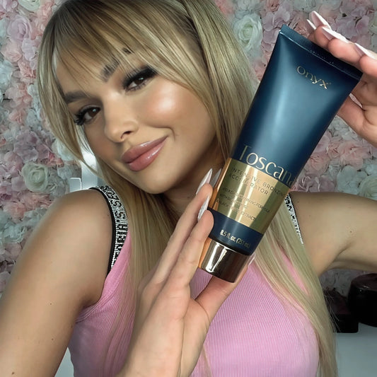 Blonde woman smiling at the camera and holding Onyx Toscana tanning cream close to her face