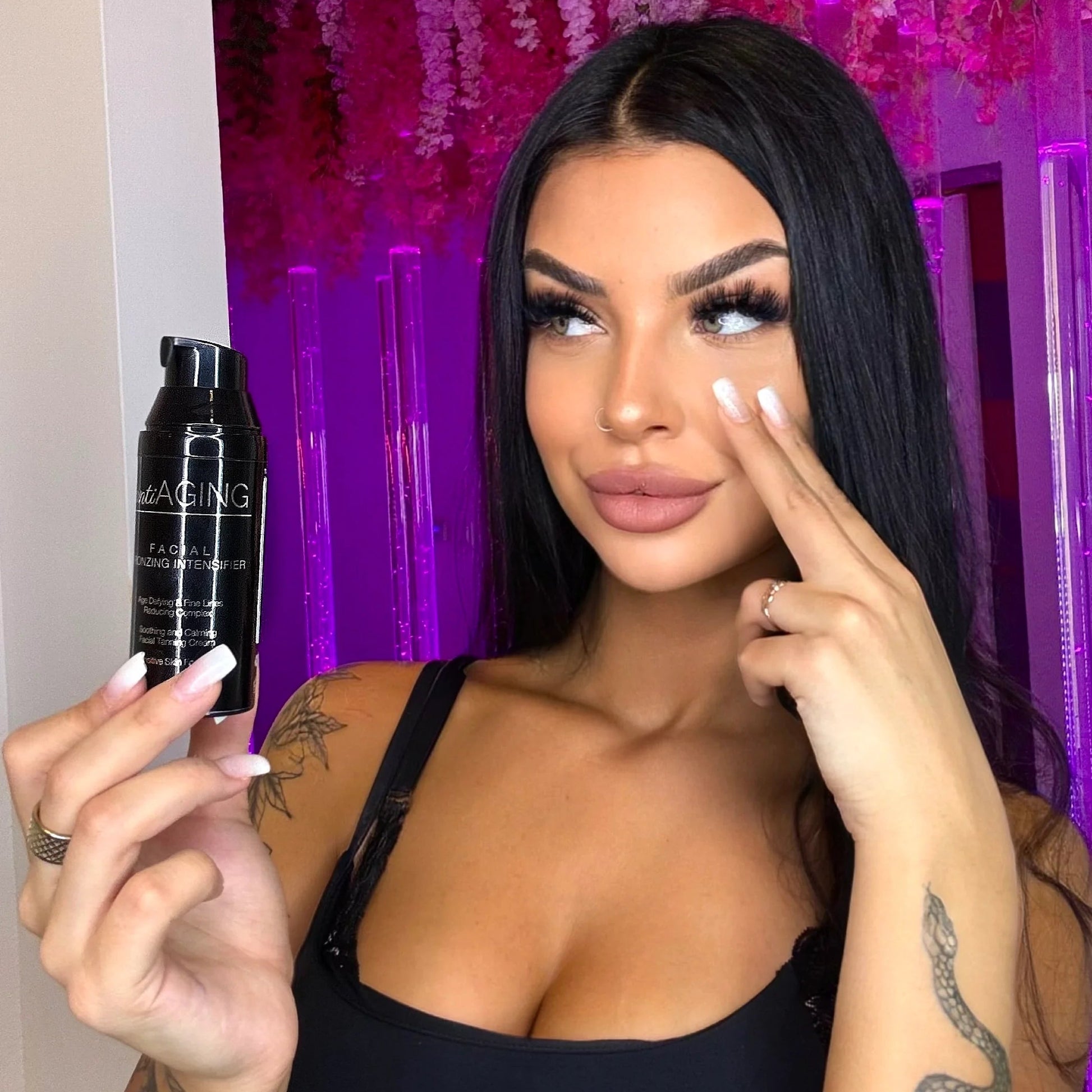 Model holding a black Onyx antiAGING Facial Bronzing Intensifier bottle beside her face, with purple lighting and hanging flowers in the background.