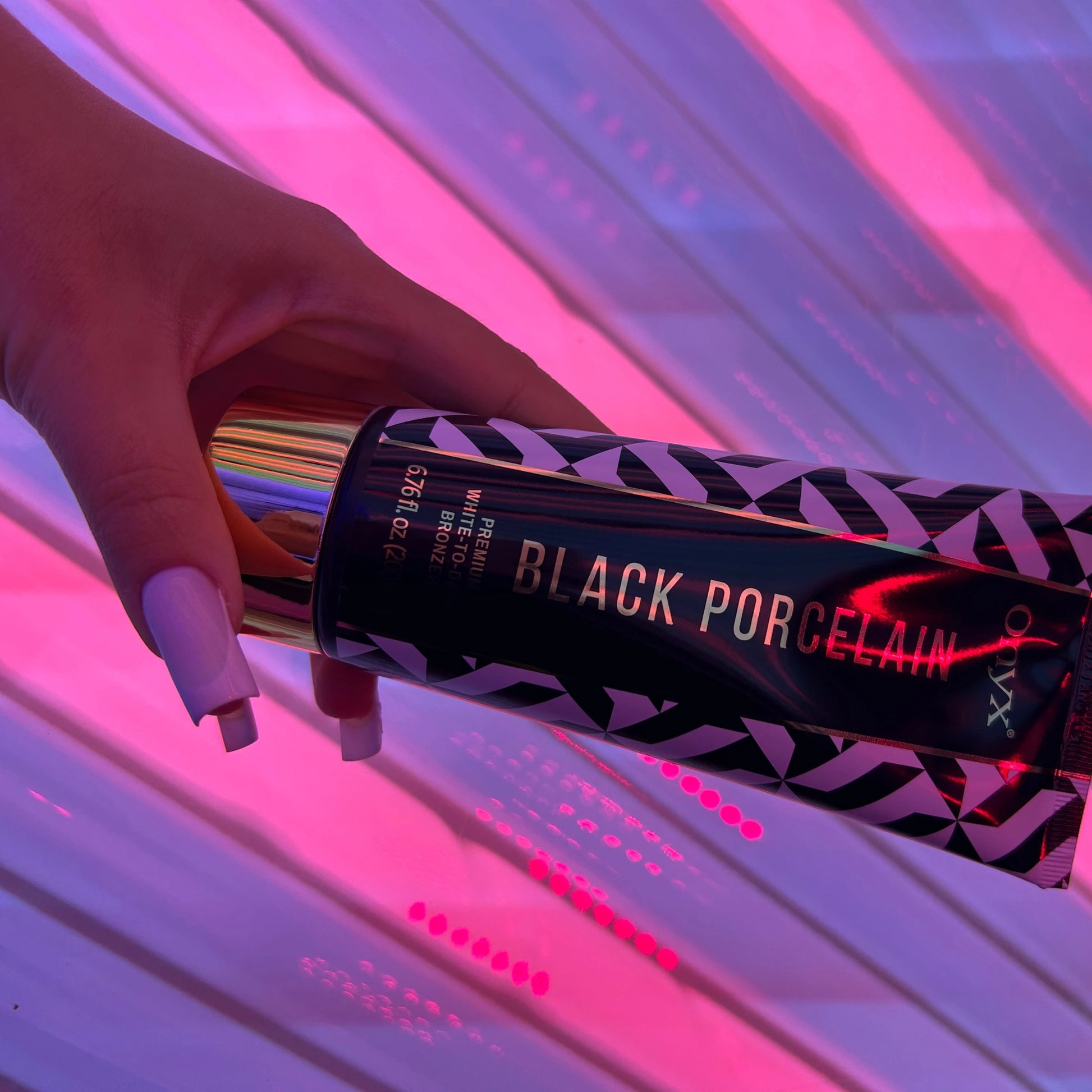Close-up of a hand with purple nails holding Onyx Black Porcelain cream under pink UV light