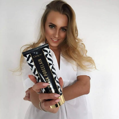 Blonde woman wearing a white blouse smiling and holding Onyx Black Porcelain cream toward the camera