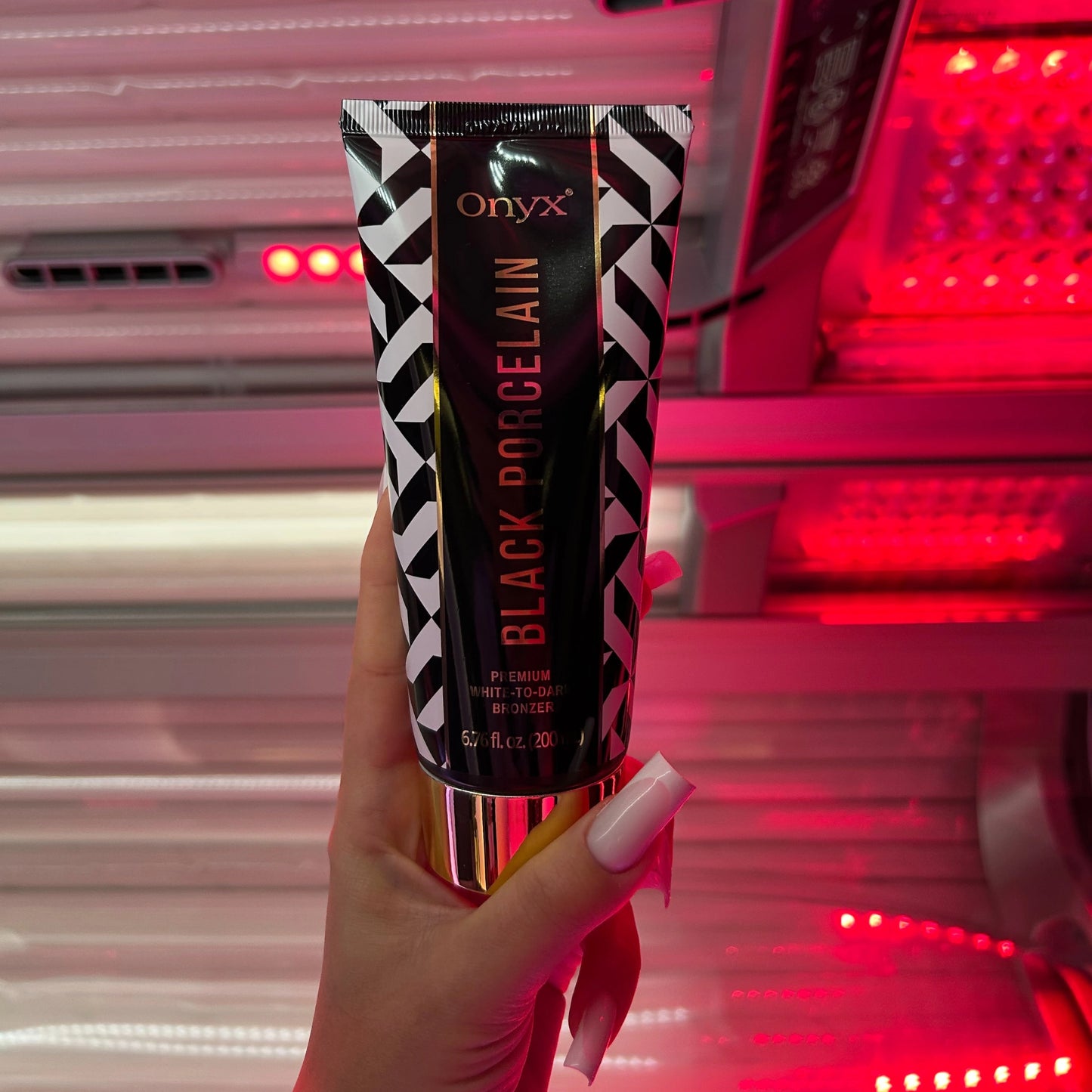 Hand with long nails holding Onyx Black Porcelain cream in front of tanning booth with red glow