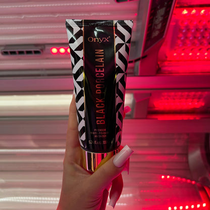 Hand with long nails holding Onyx Black Porcelain cream in front of tanning booth with red glow