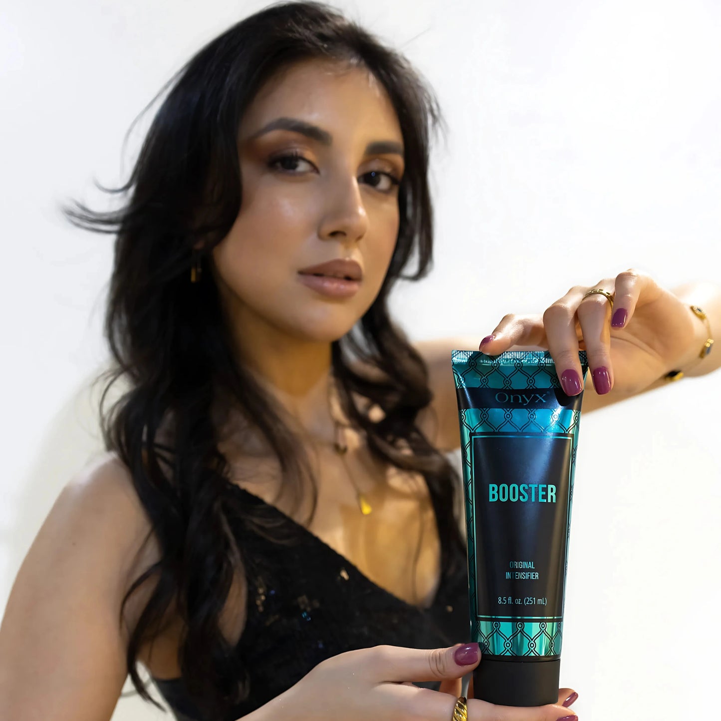 Close-up portrait of woman holding Onyx Booster sunbed accelerator cream, glam indoor lighting