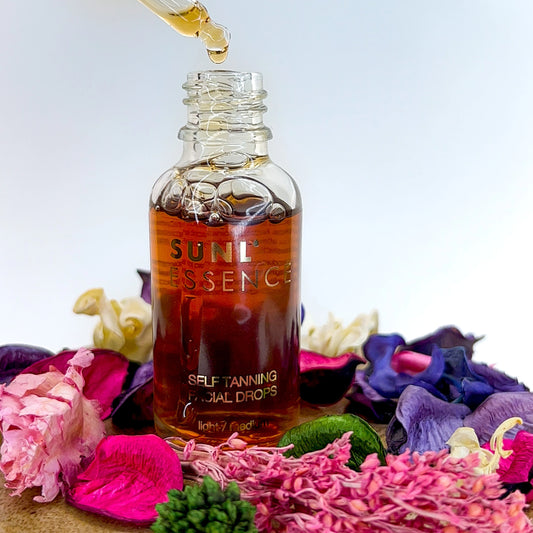 Glass bottle of self-tanning facial drops surrounded by colourful dried flowers on a white background