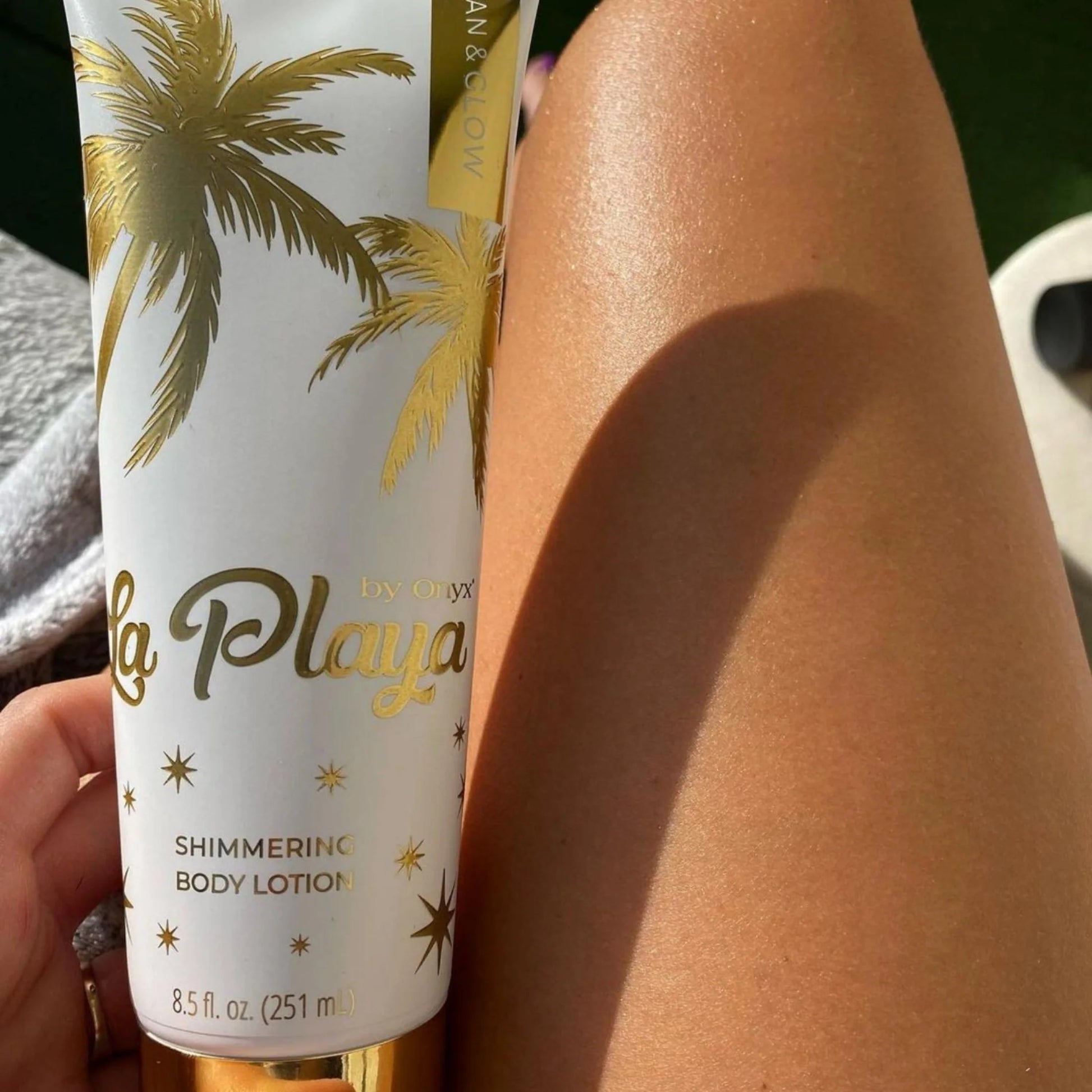 Close-up of a tanned leg in sunlight with a tube of shimmering body cream placed on top of the skin