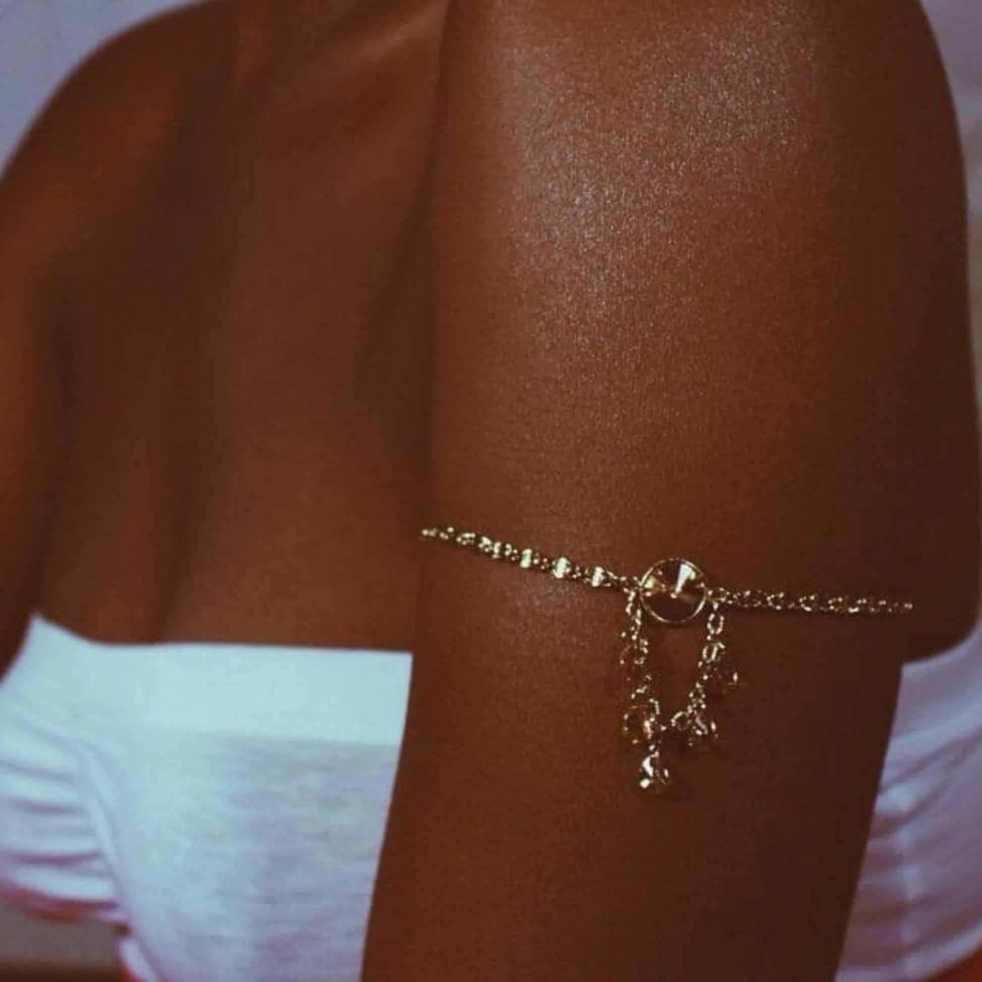 Close-up of a bronzed arm with a gold shimmer bracelet visible on the skin under soft lighting