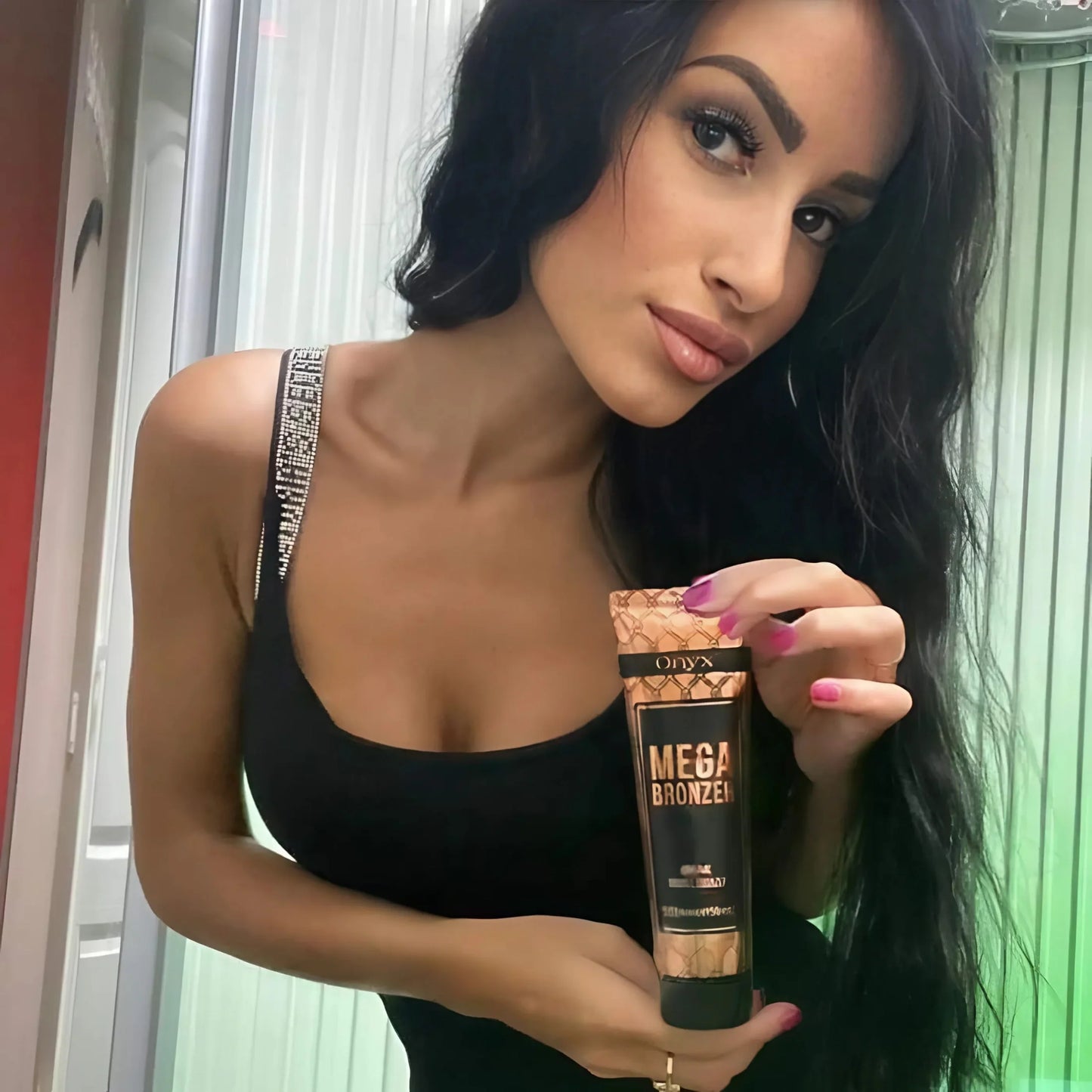 Stylish brunette in a black outfit posing with Onyx Mega Bronzer sunbed cream, green lighting behind her