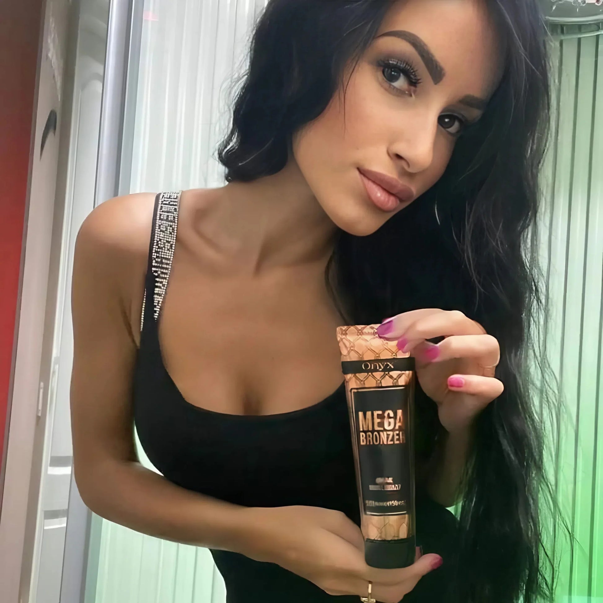 Stylish brunette in a black outfit posing with Onyx Mega Bronzer sunbed cream, green lighting behind her