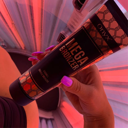 Hand with purple nails holding Onyx Mega Bronzer lotion under red lights inside a tanning bed