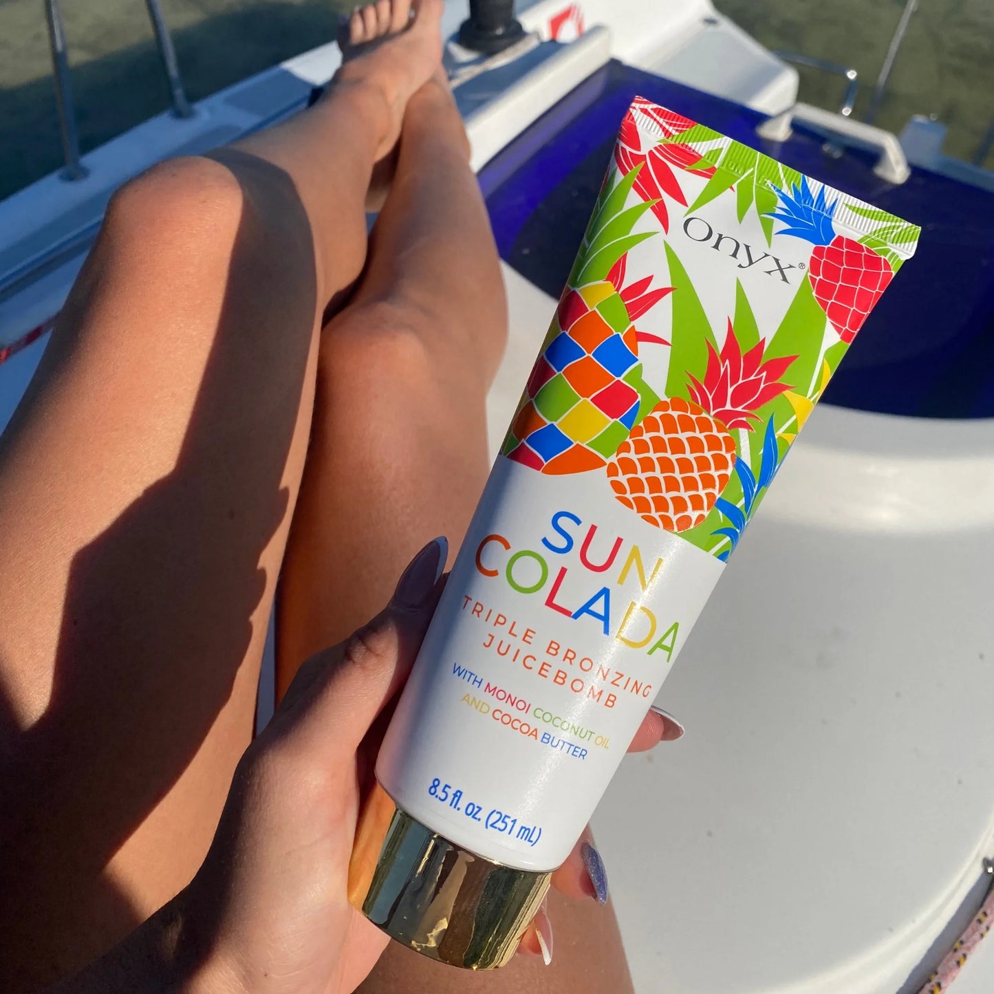 Onyx Suncolada sunbed accelerator cream displayed on tanned legs in sunlight on yacht