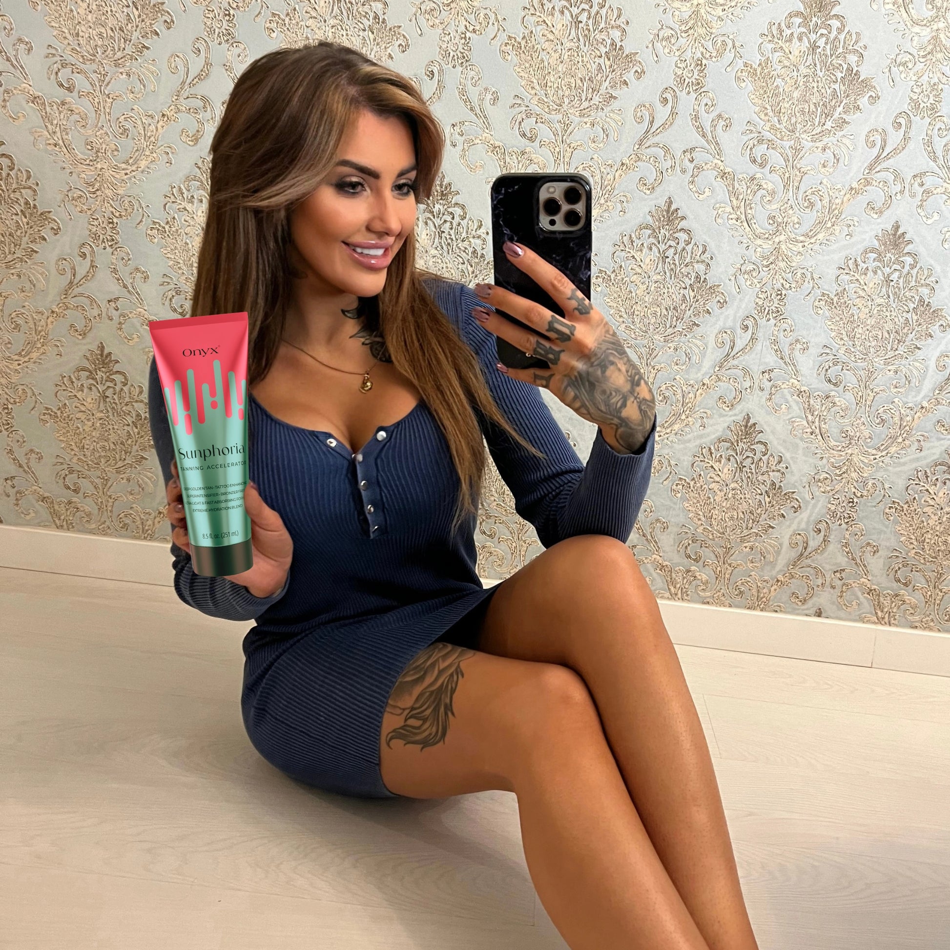 Tattooed woman taking mirror selfie with Onyx Sunphoria sunbed tanning accelerator cream