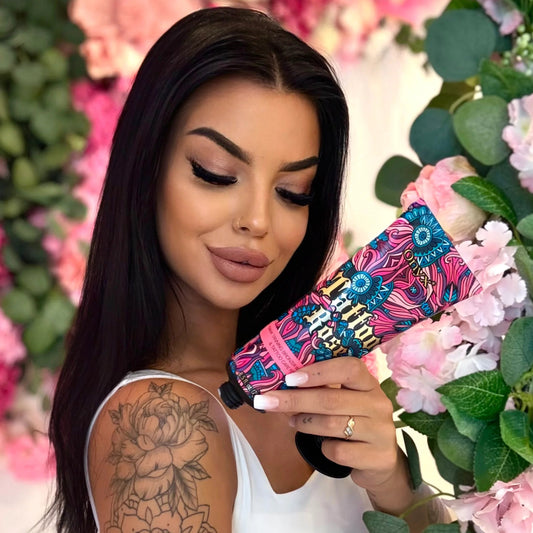 Model holding an Onyx Tattoo Rose bronzer cream tube beside a display of pink flowers.