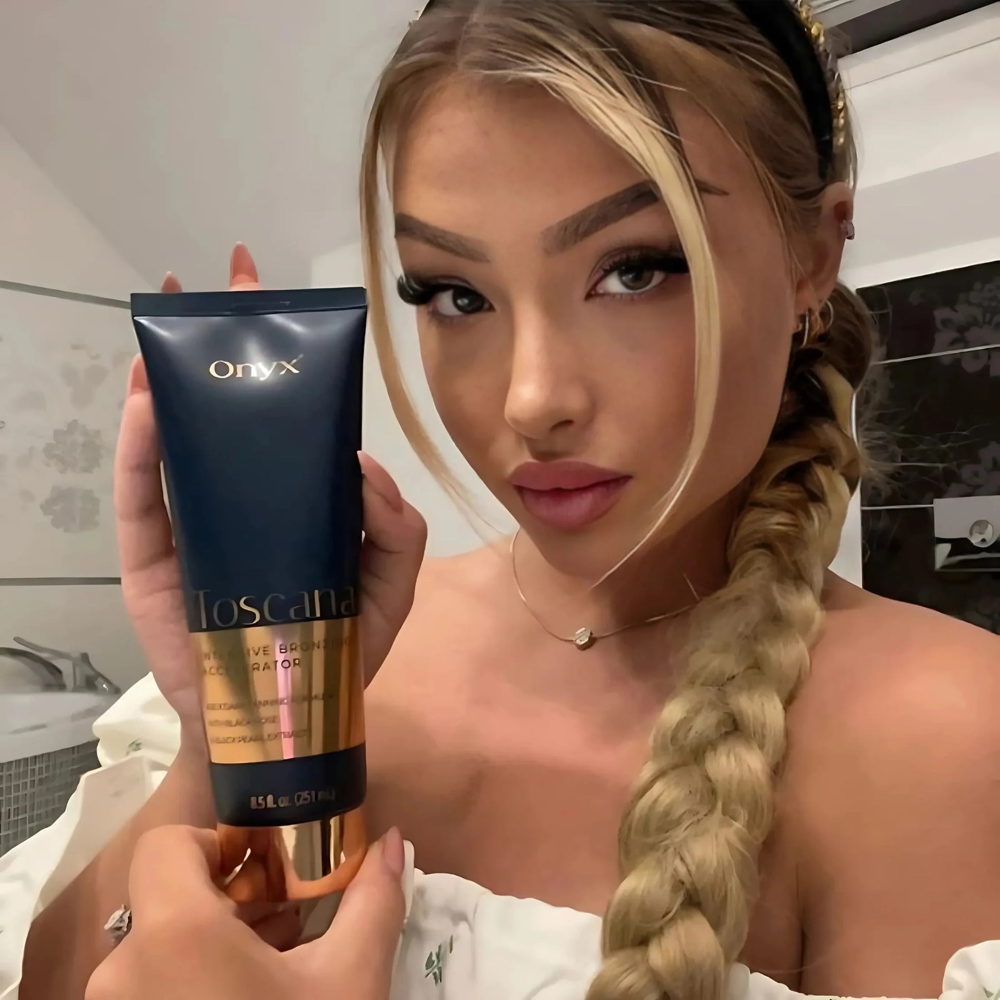Blonde woman posing in a bathroom holding Onyx Toscana bronzing cream