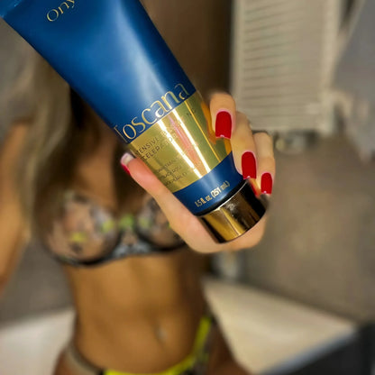 Close-up of Onyx Toscana tanning cream held forward, with a blurred woman in a bikini in the background