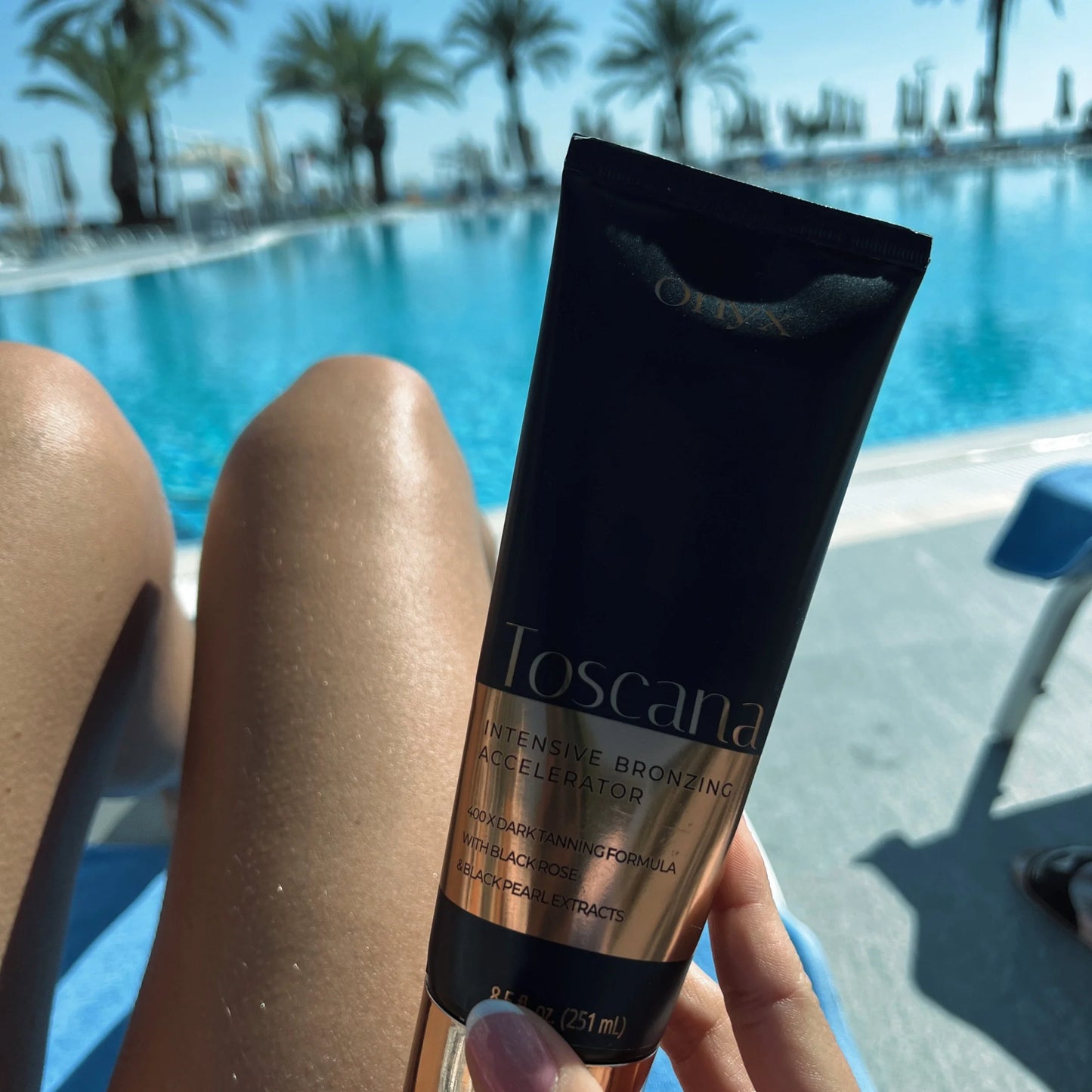 Woman relaxing by a pool holding Onyx Toscana bronzing cream with tanned legs in sunlight