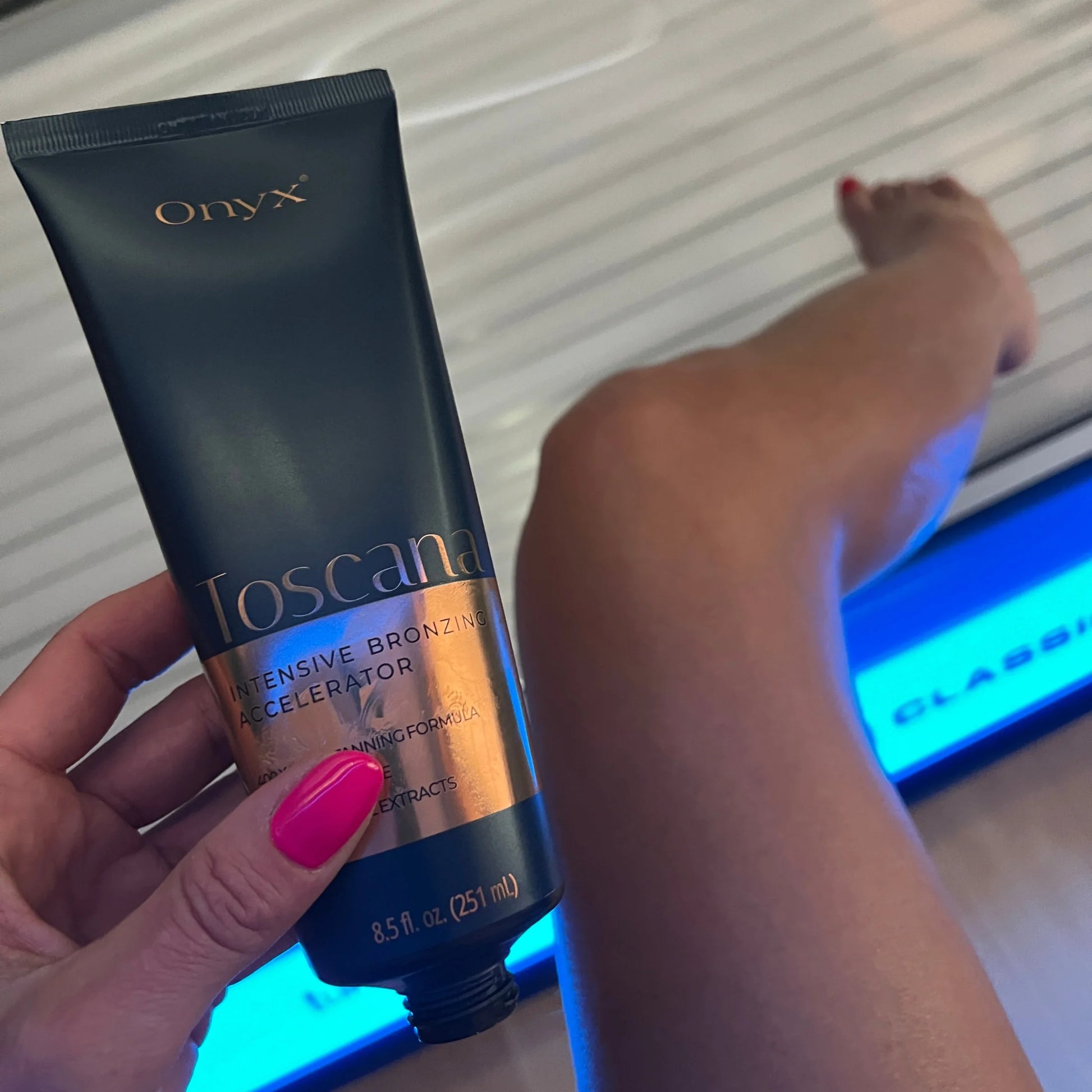 Open Onyx Toscana bronzing cream held in hand with a tanned leg visible in the background