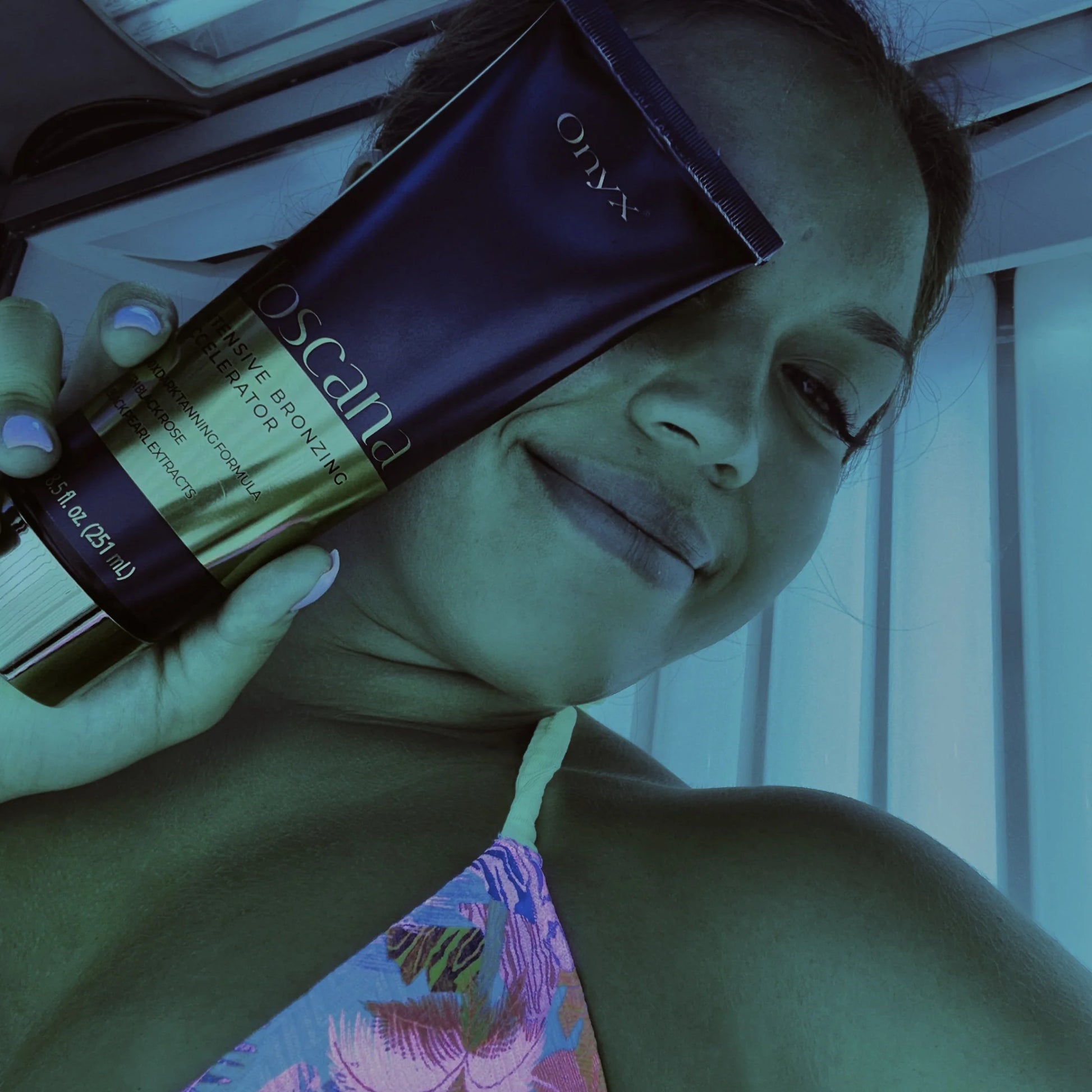Woman smiling inside a sunbed holding Onyx Toscana bronzing cream beside her face