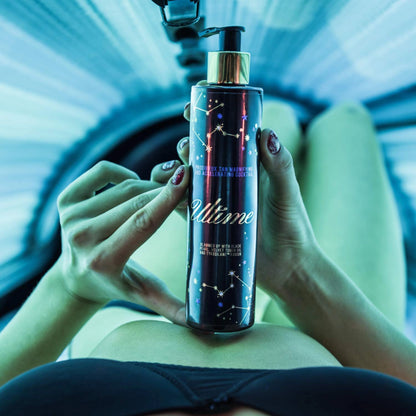 Woman lying inside tanning bed holding Onyx Ultime tanning cream, blue UV light reflecting on the bottle