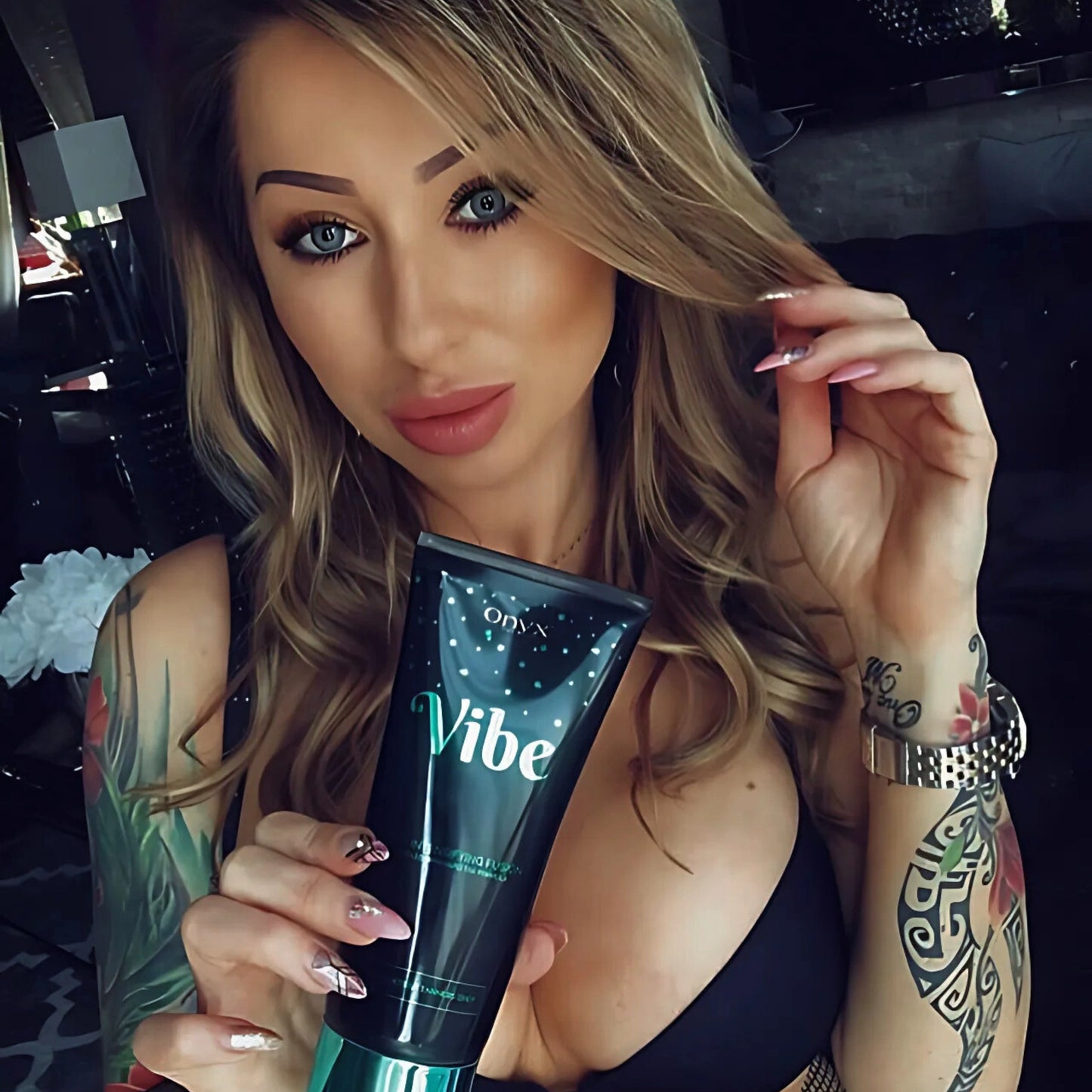 Woman holding Onyx Vibe sunbed accelerator cream close-up with tattoos visible on her arm