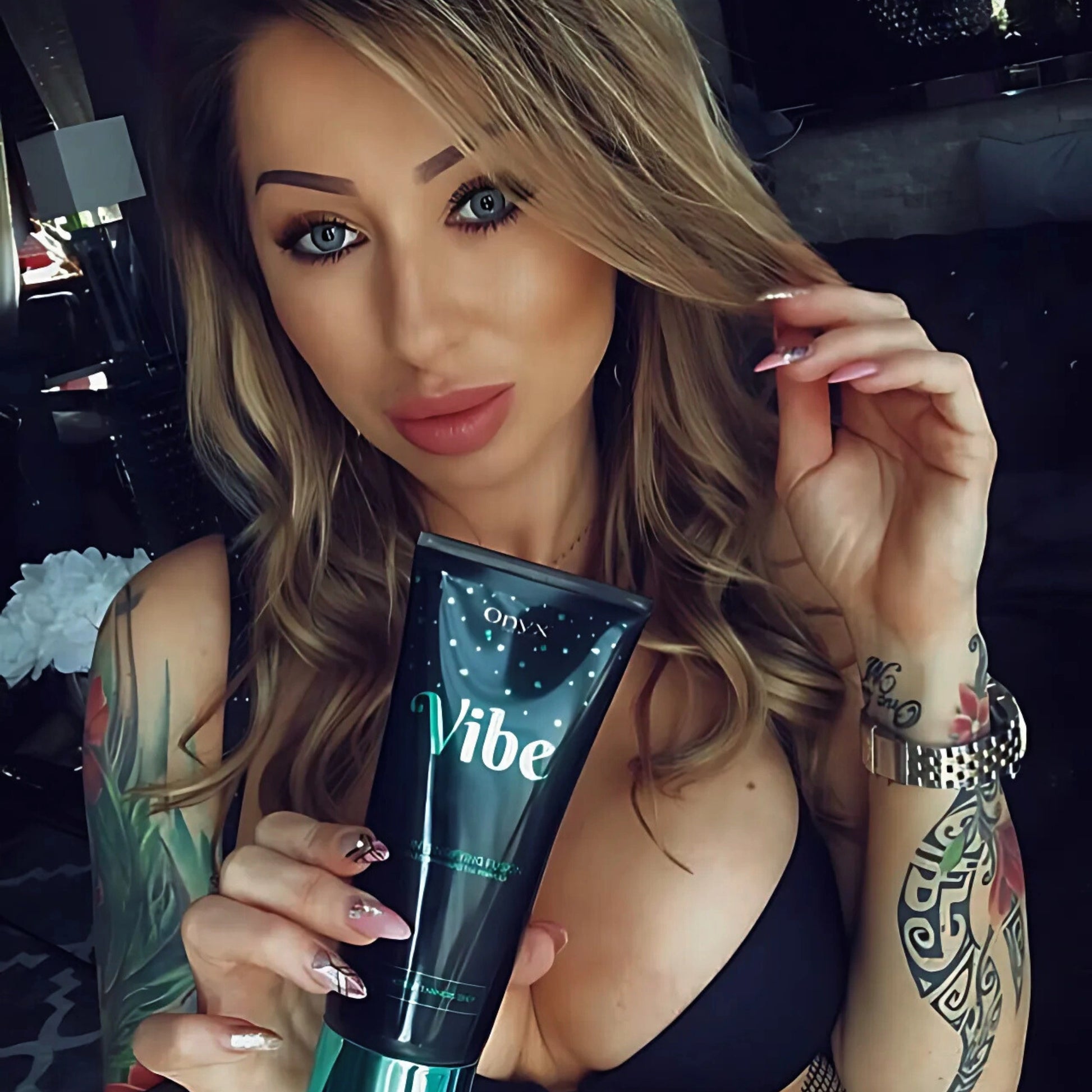 Woman holding Onyx Vibe sunbed accelerator cream close-up with tattoos visible on her arm