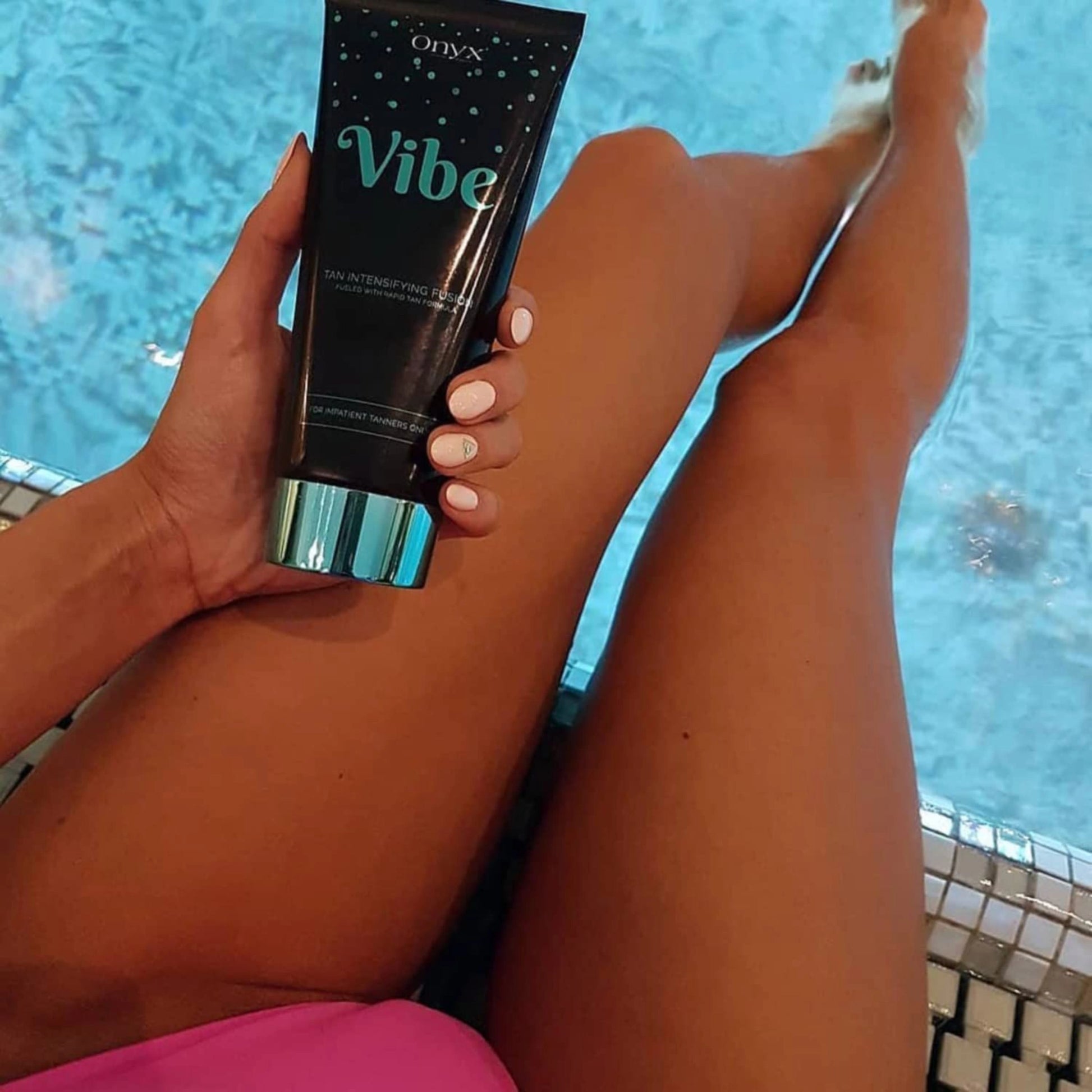 Onyx Vibe tanning accelerator cream in hand by the poolside with bronzed legs visible