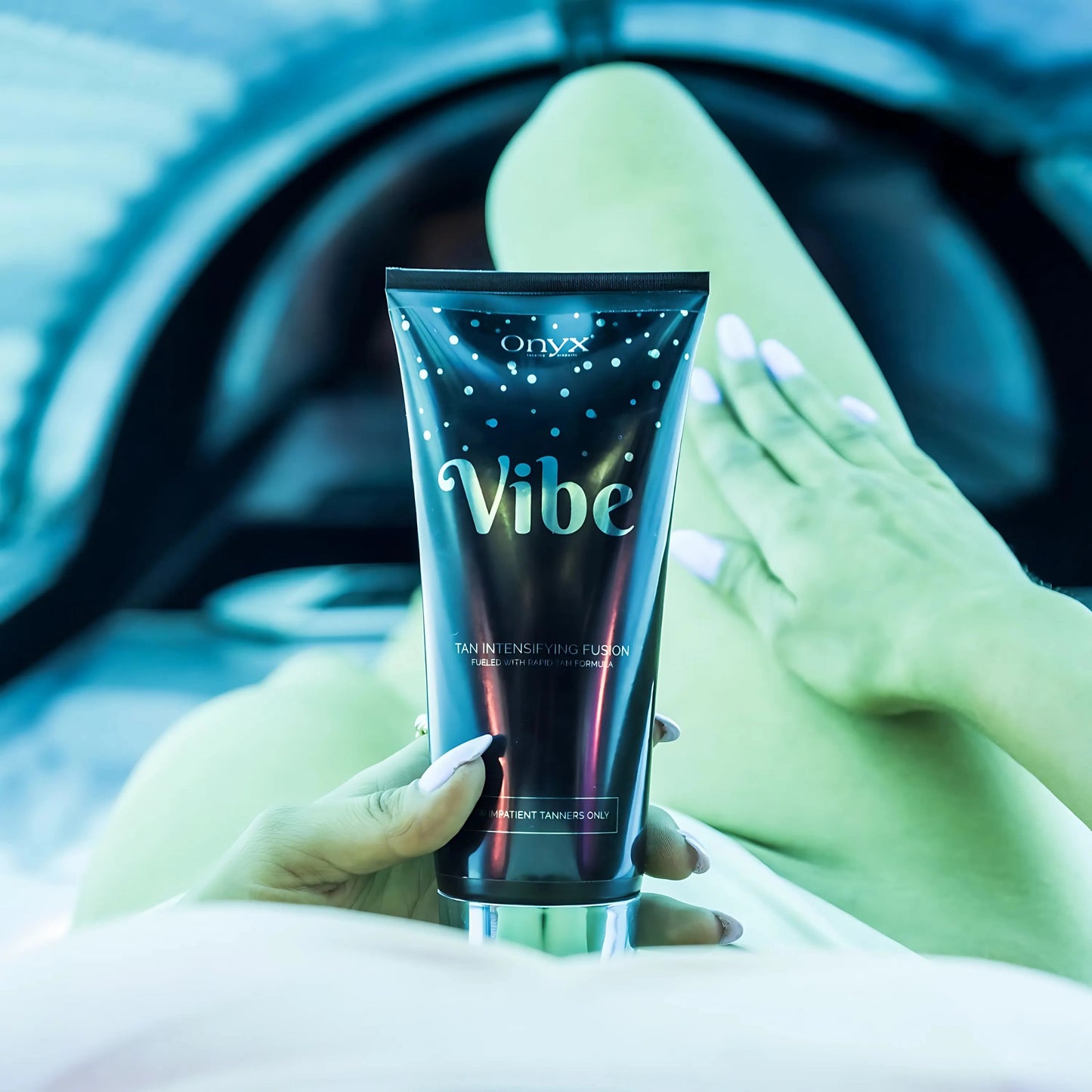 Onyx Vibe sunbed accelerator cream held in hand inside tanning bed with UV lights glowing