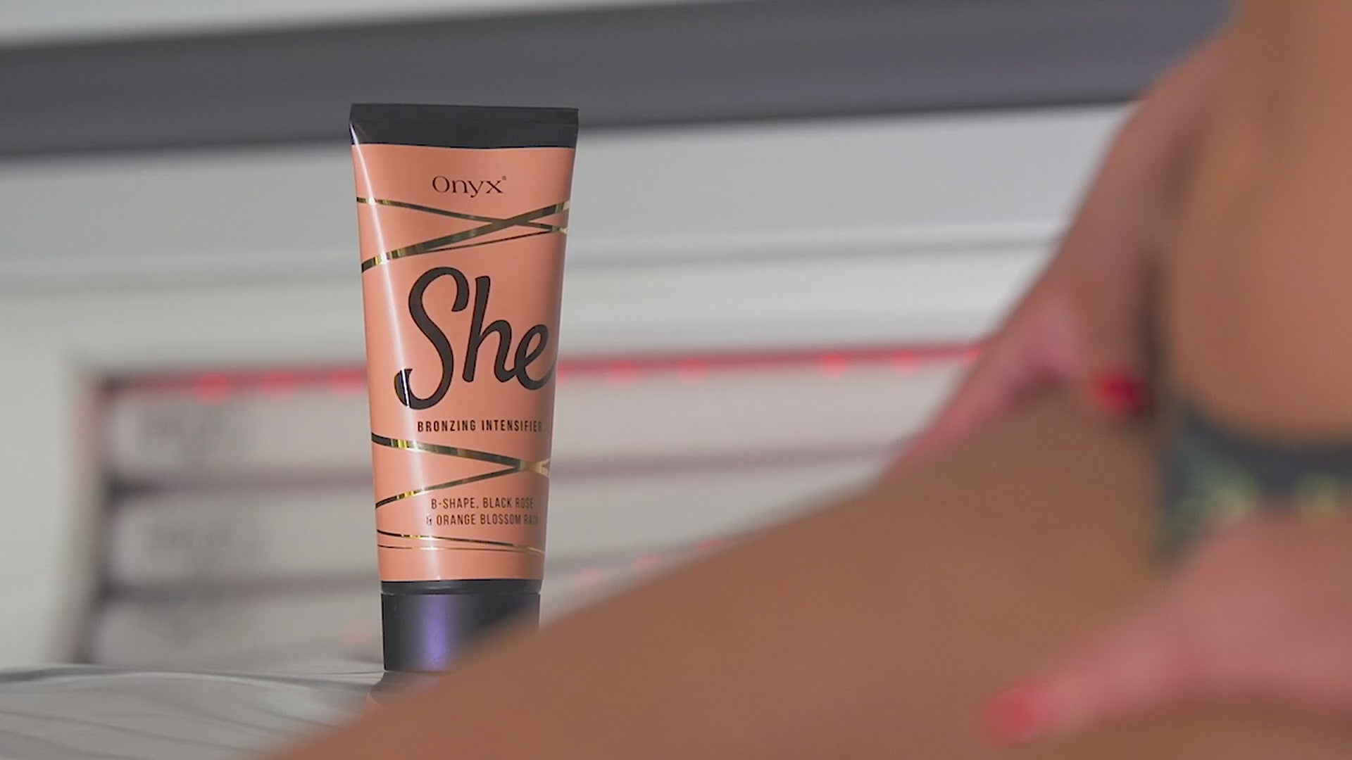 Women applying Onyx She tanning cream, showing smooth glowing skin and the product tube in bright, elegant surroundings