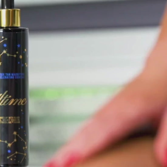 Woman in blue bikini sitting in tanning bed, smiling while applying Onyx Ultime tanning cream under natural light