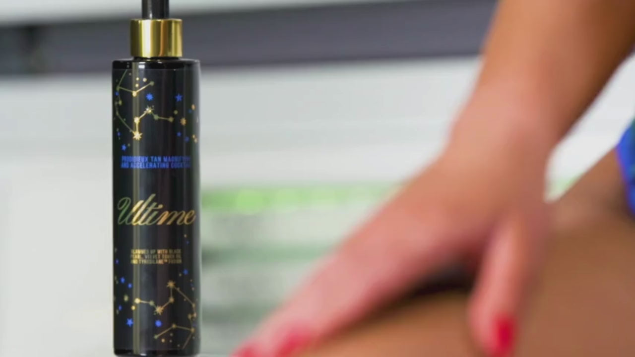 Woman in blue bikini sitting in tanning bed, smiling while applying Onyx Ultime tanning cream under natural light