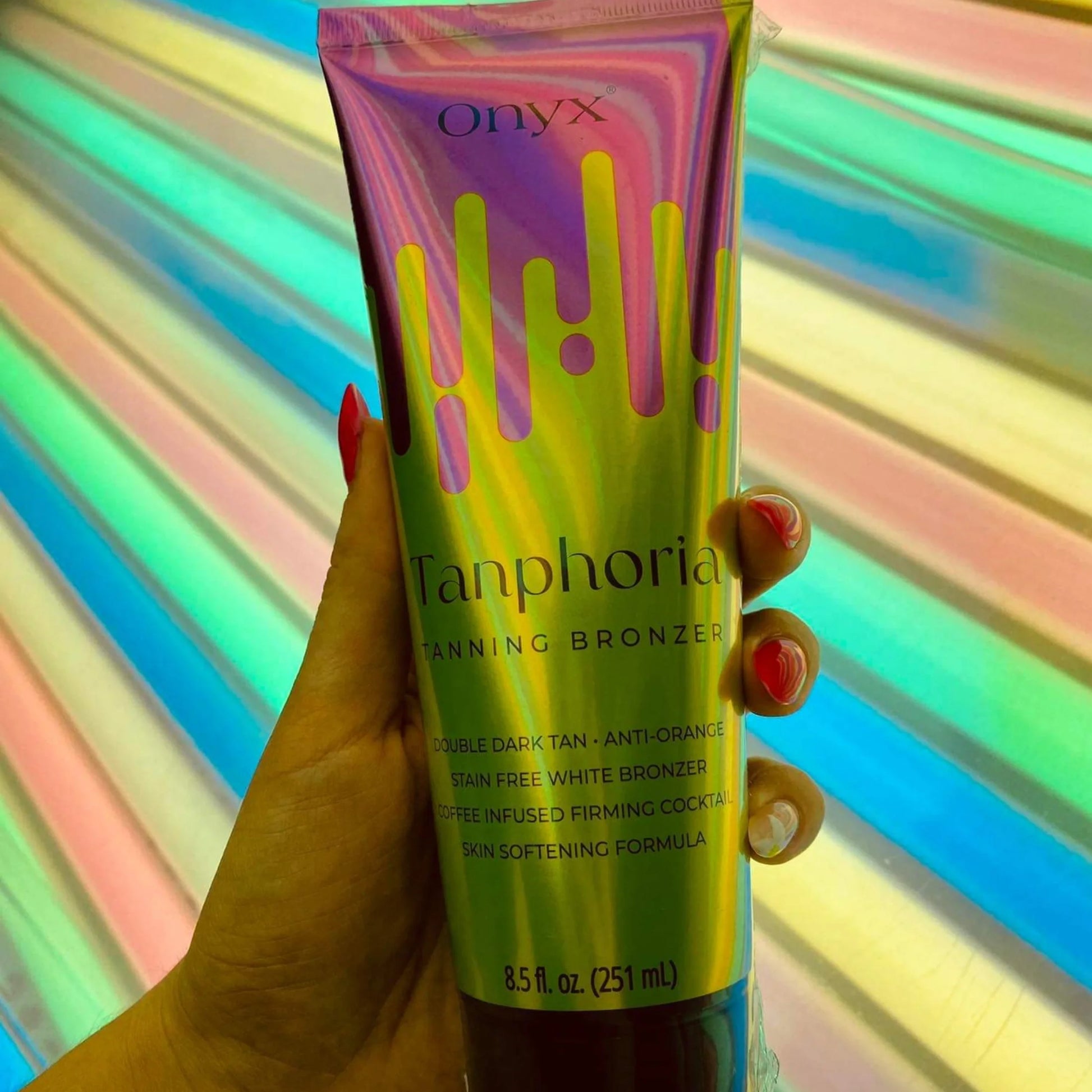 Tanphoria Tanning Bronzer tube held in hand inside a tanning bed, surrounded by colourful glowing lights.