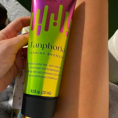 Close-up of a person’s bronzed leg holding a Tanphoria Tanning Bronzer tube, showing even tan colour and smooth skin.
